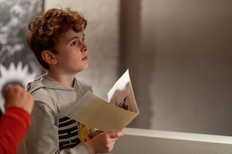 Op deze afbeelding zie je: Een kind die de tentoonstelling bezoek van A Closser Look van Carla Kogelman in het Kinderpanel en hij staart naar voren met een boekje in zijn hand. Deze foto is gemaakt door Ralf Silvius