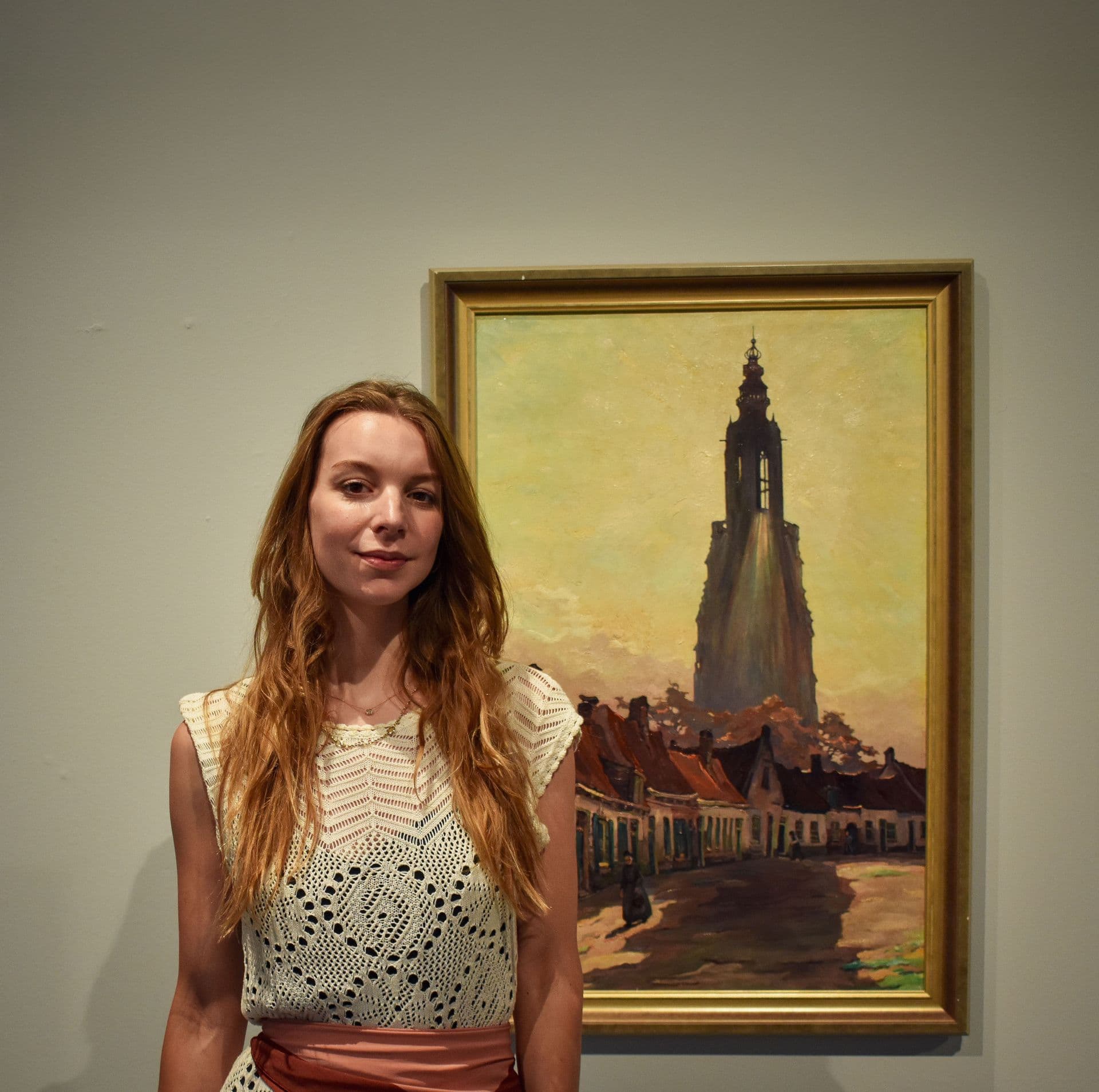 Op deze afbeelding zie je: Een foto van Dorine in witte kleding die staat voor een schilderij van Amersfoort. Het is een pers foto en deze foto is gemaakt in Museum Amersfoort en gemaakt door Vana Fotografie.
